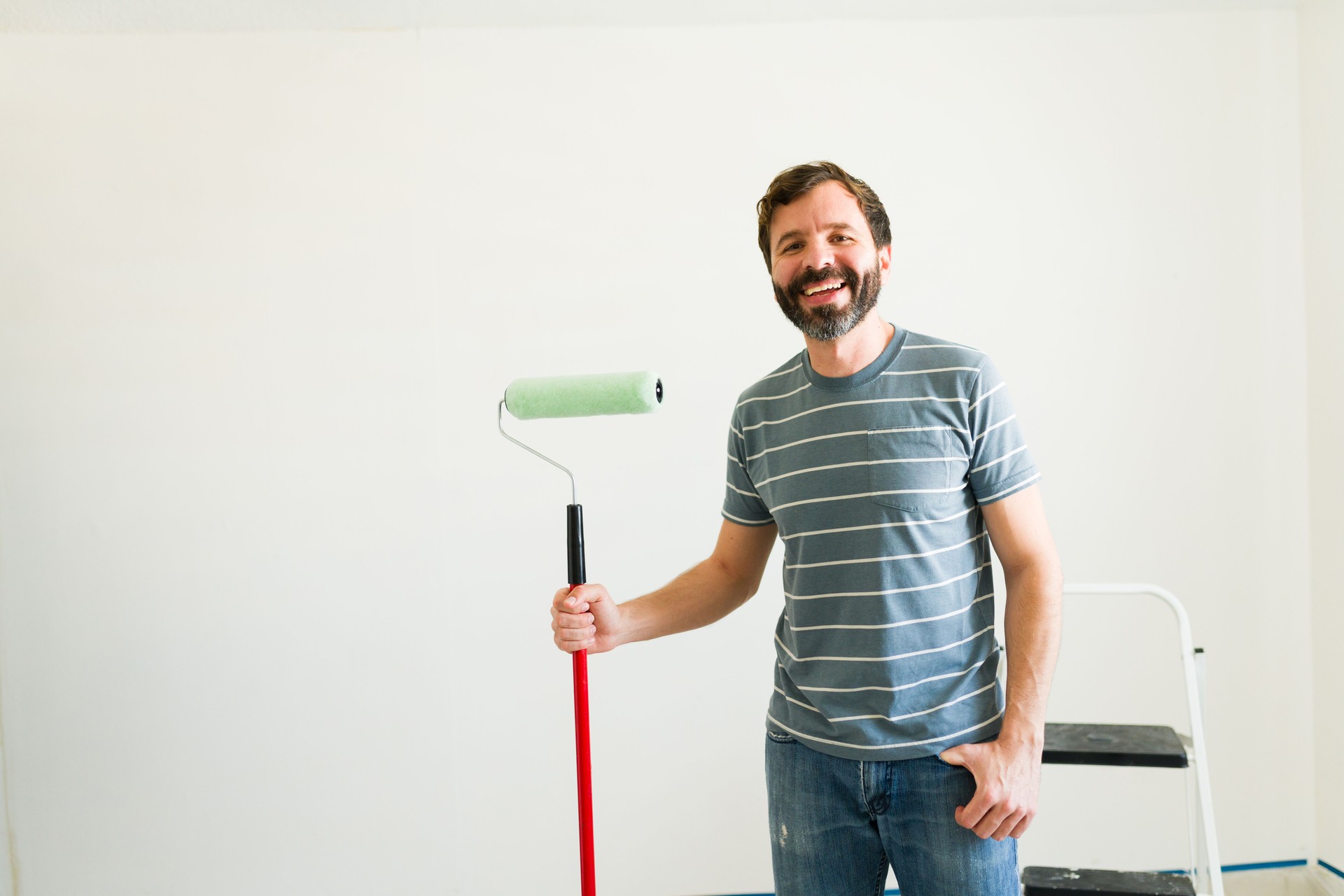 Cheerful handyman holds a paint roller in an empty room, eager to begin painting